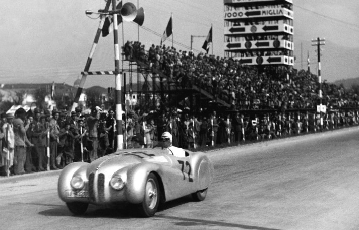 Period photograph of a streamlined BMW 328 racing car on track with spectators lining the circuit