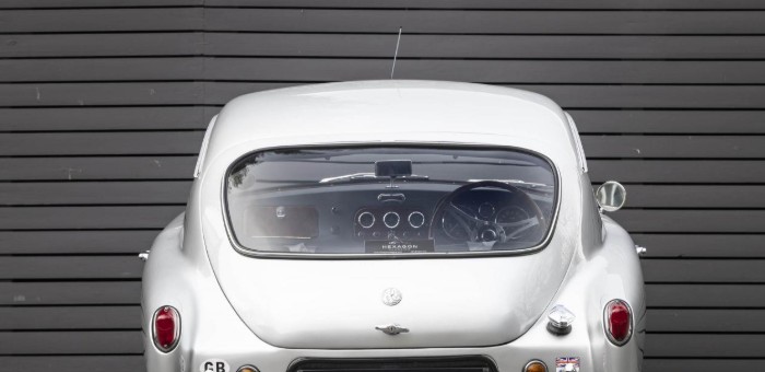 Rear view of an AC Aceca showing the fastback tailgate and curved rear screen against dark horizontal cladding