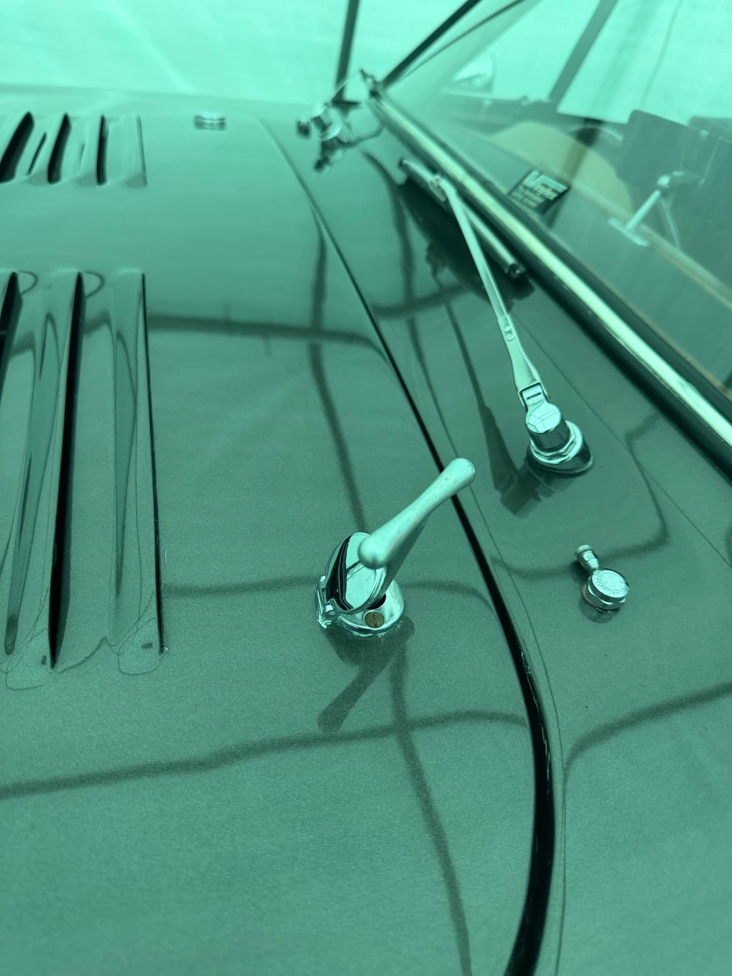Chromed bonnet catch lever on the top of an AC Aceca's bonnet, next to the wiper spindle and the windscreen shut-line.