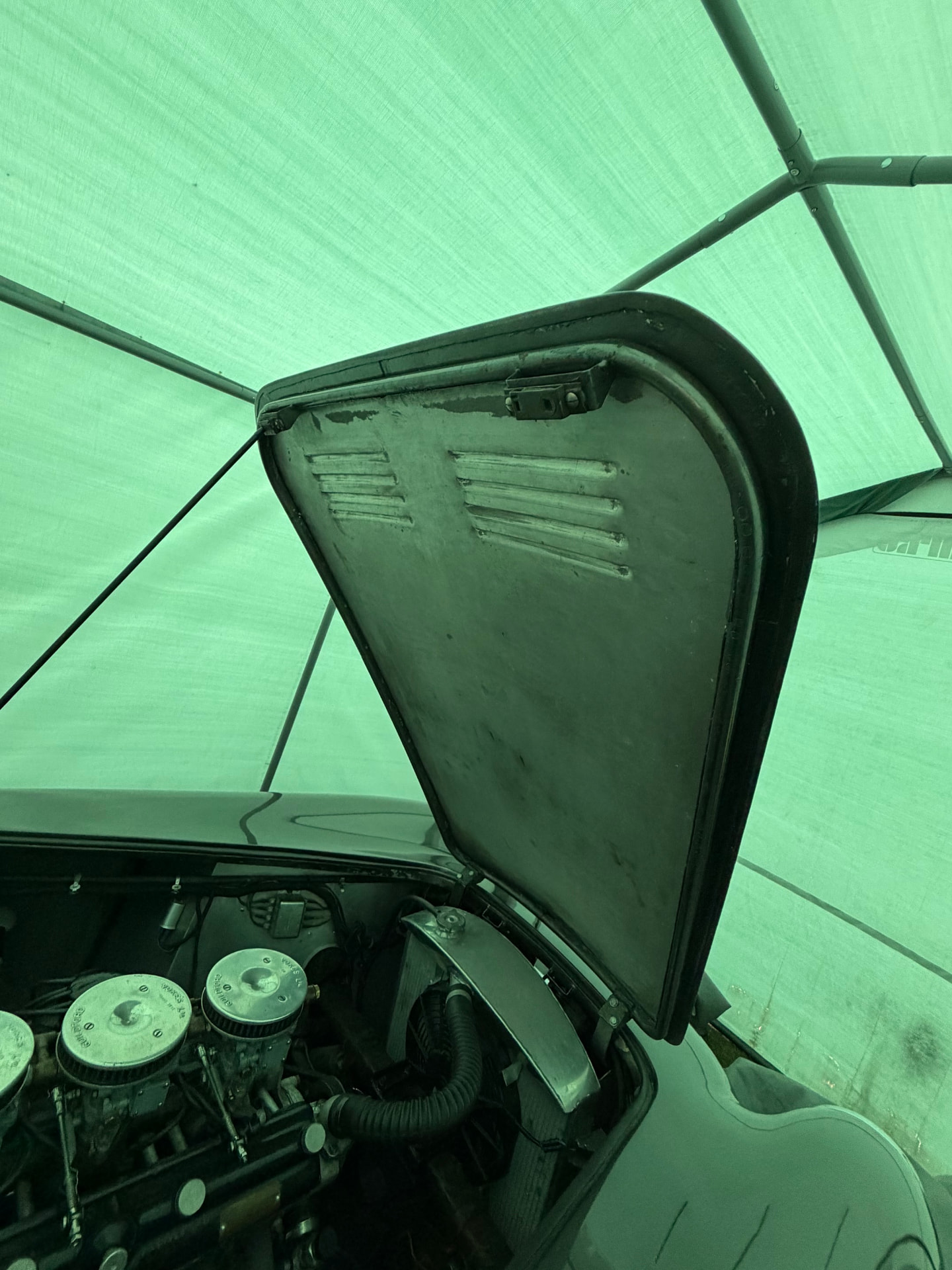 AC Aceca bonnet raised and held open by a single slim steel prop rod, seen from inside the engine bay with the louvred underside of the alloy panel above.