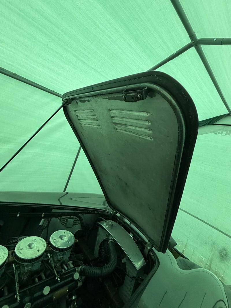 AC Aceca bonnet raised and held open by a single slim steel prop rod, seen from inside the engine bay with the louvred underside of the alloy panel above.